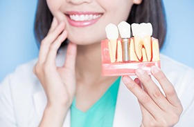 Smiling Lebanon implant dentist holding model of dental implants