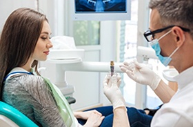 Smiling woman holding model with dental implant and crown