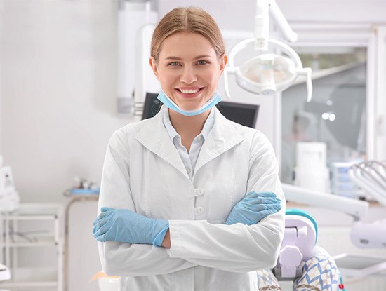 Smiling dentist standing in treatment room with arms crossed