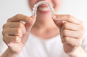 Woman in white t-shirt holding Invisalign aligner