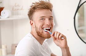 Smiling young man brushing his teeth