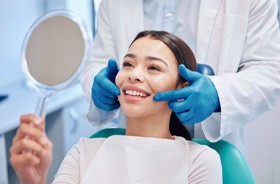 Patient holding mirror, looking at her teeth during smile makeover consultation