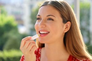 Woman standing outdoors, applying lip balm