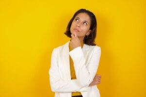 Woman wearing a curious expression as she stands against yellow background